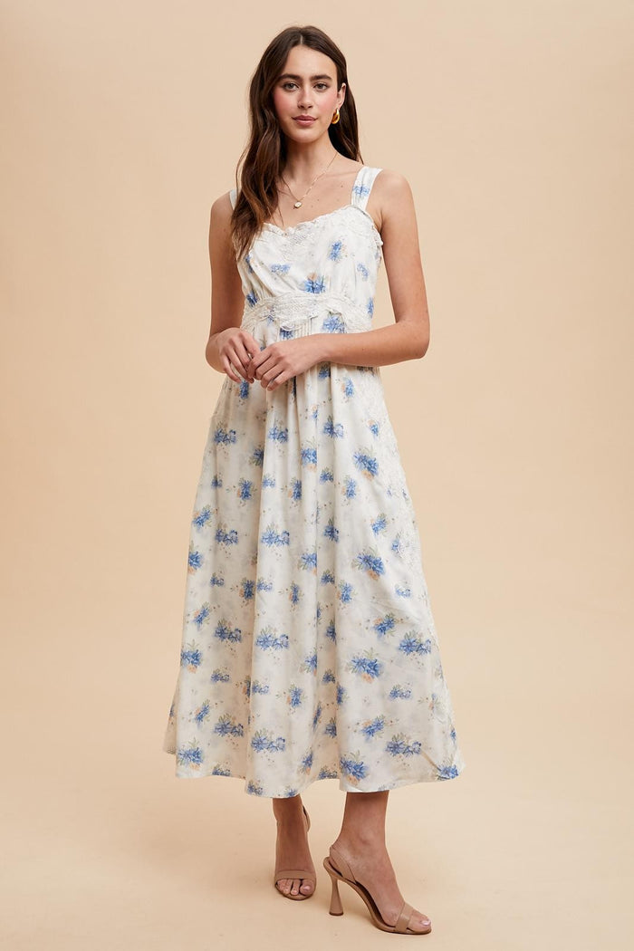 woman wearing a floral print midi dress with blue and white colors, featuring adjustable straps and a fitted bodice