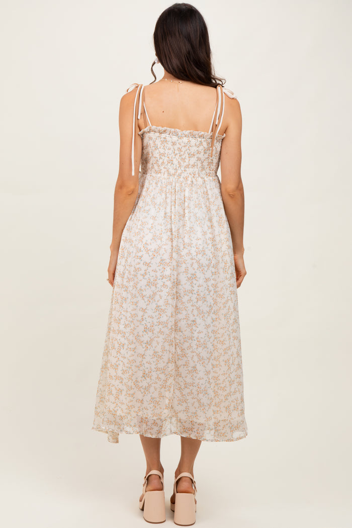 woman wearing a light floral midi dress with smocked bodice and tie shoulder straps, standing with back to the camera