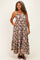 woman wearing a brown floral maxi dress with spaghetti straps and a tiered skirt, standing and smiling