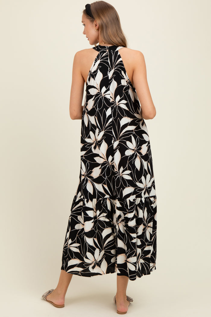 woman wearing a black and white floral print maternity maxi dress with a halter neck and tiered skirt from the back