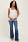 woman wearing a beige maternity tank top and blue flared jeans, holding her baby bump
