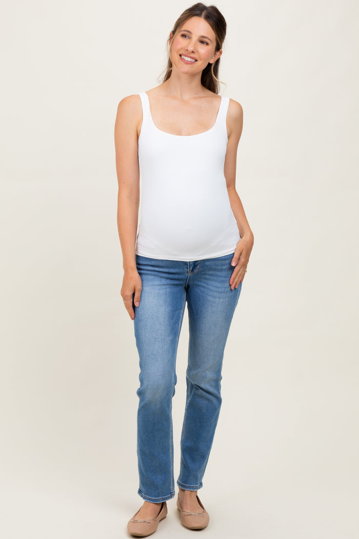 woman wearing a white maternity tank top and blue jeans, showing a visible baby bump