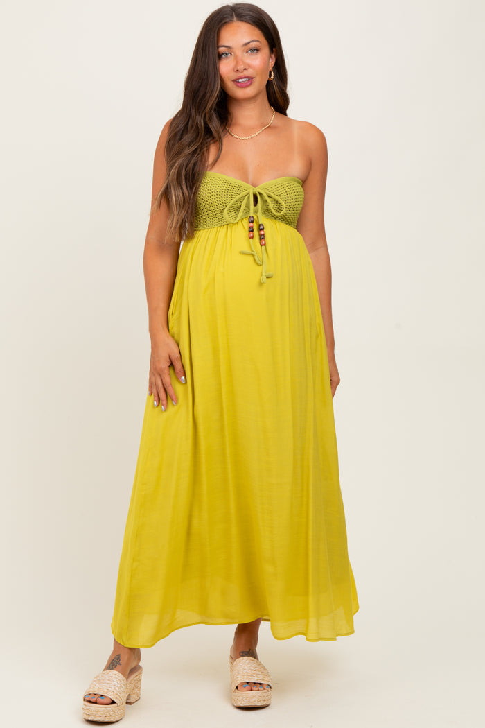 woman wearing a yellow maternity maxi dress with a crocheted bodice and tie detail, showing her baby bump