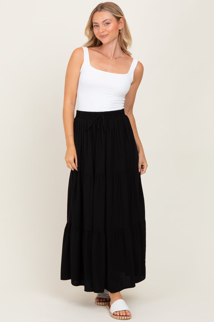 woman wearing a white square neck tank top and a black tiered maxi skirt, standing and smiling