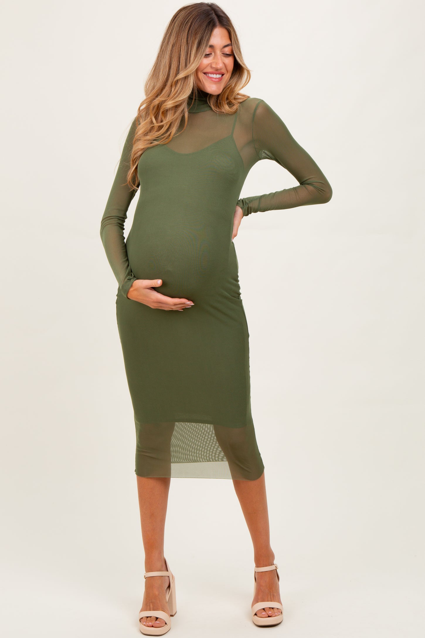 woman wearing a fitted olive green maternity dress with sheer long sleeves and a baby bump visible