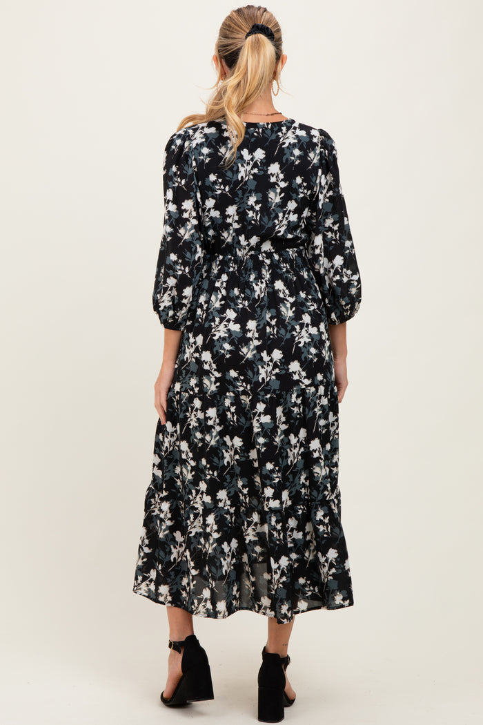 woman wearing a floral black maternity dress with three-quarter sleeves and a tiered skirt, showing her baby bump from the back