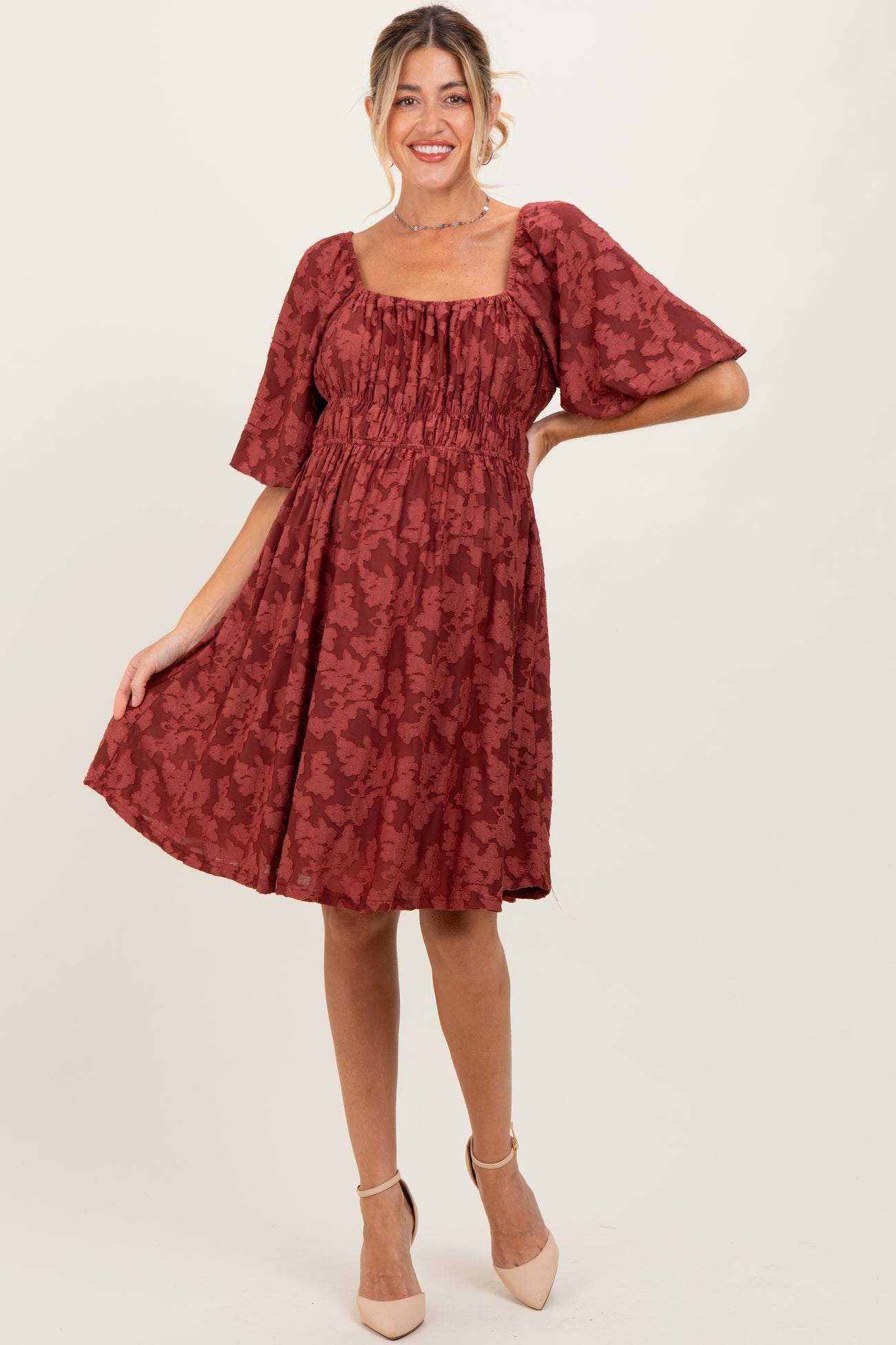 woman wearing a rust floral maternity dress with puff sleeves and a smocked bodice, showcasing her baby bump