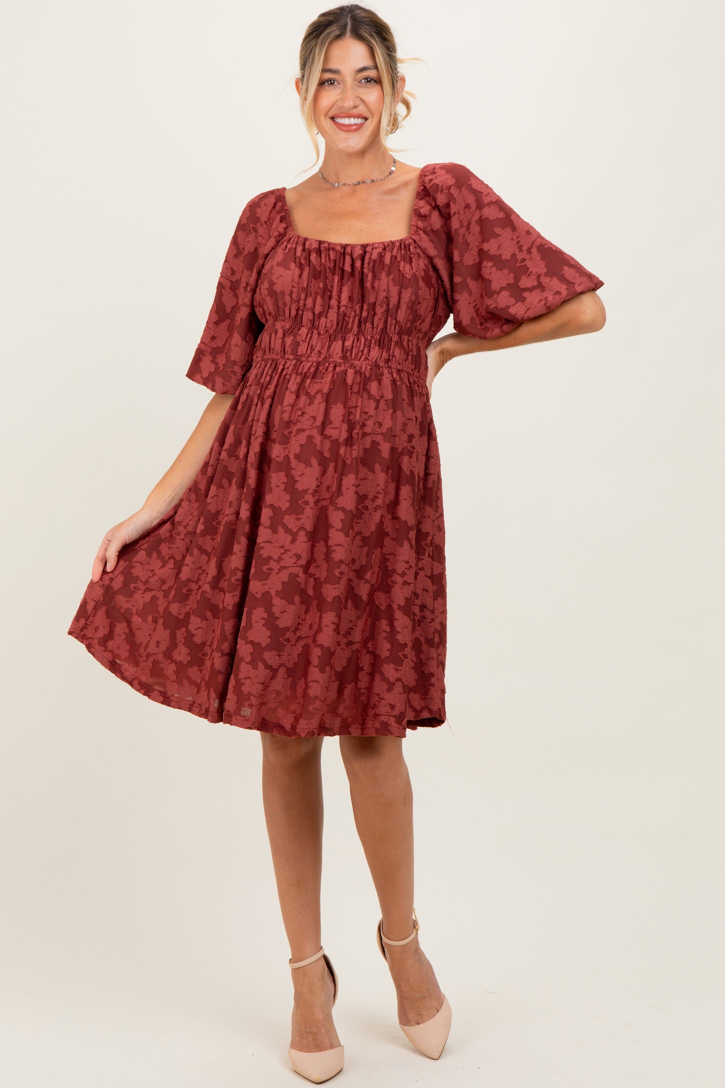 woman wearing a rust floral maternity dress with puff sleeves and a smocked bodice, showcasing her baby bump