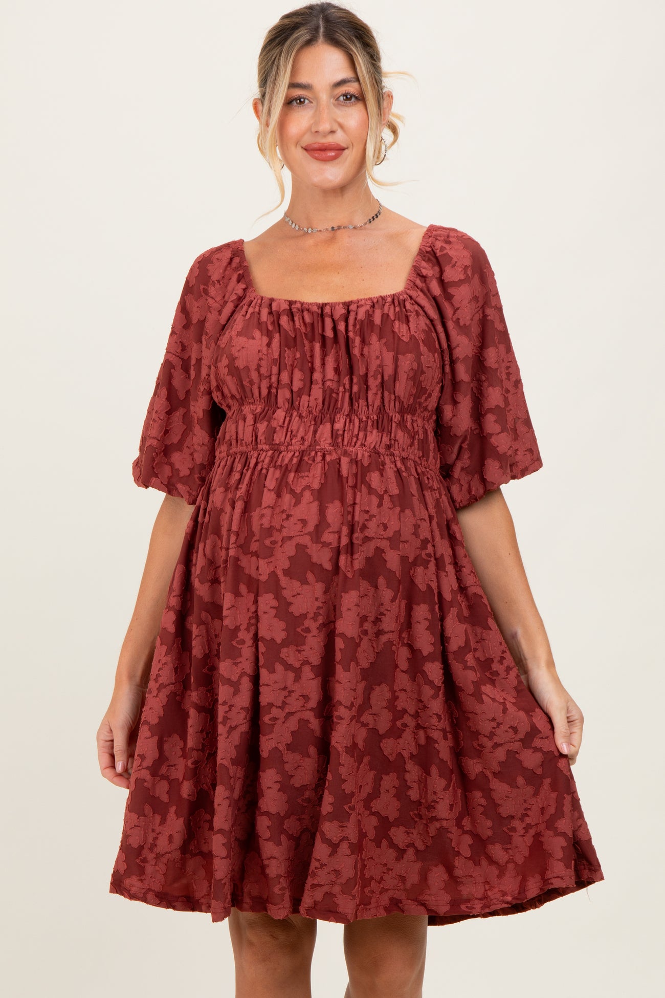 woman wearing a rust colored floral print maternity dress with square neckline and puff sleeves