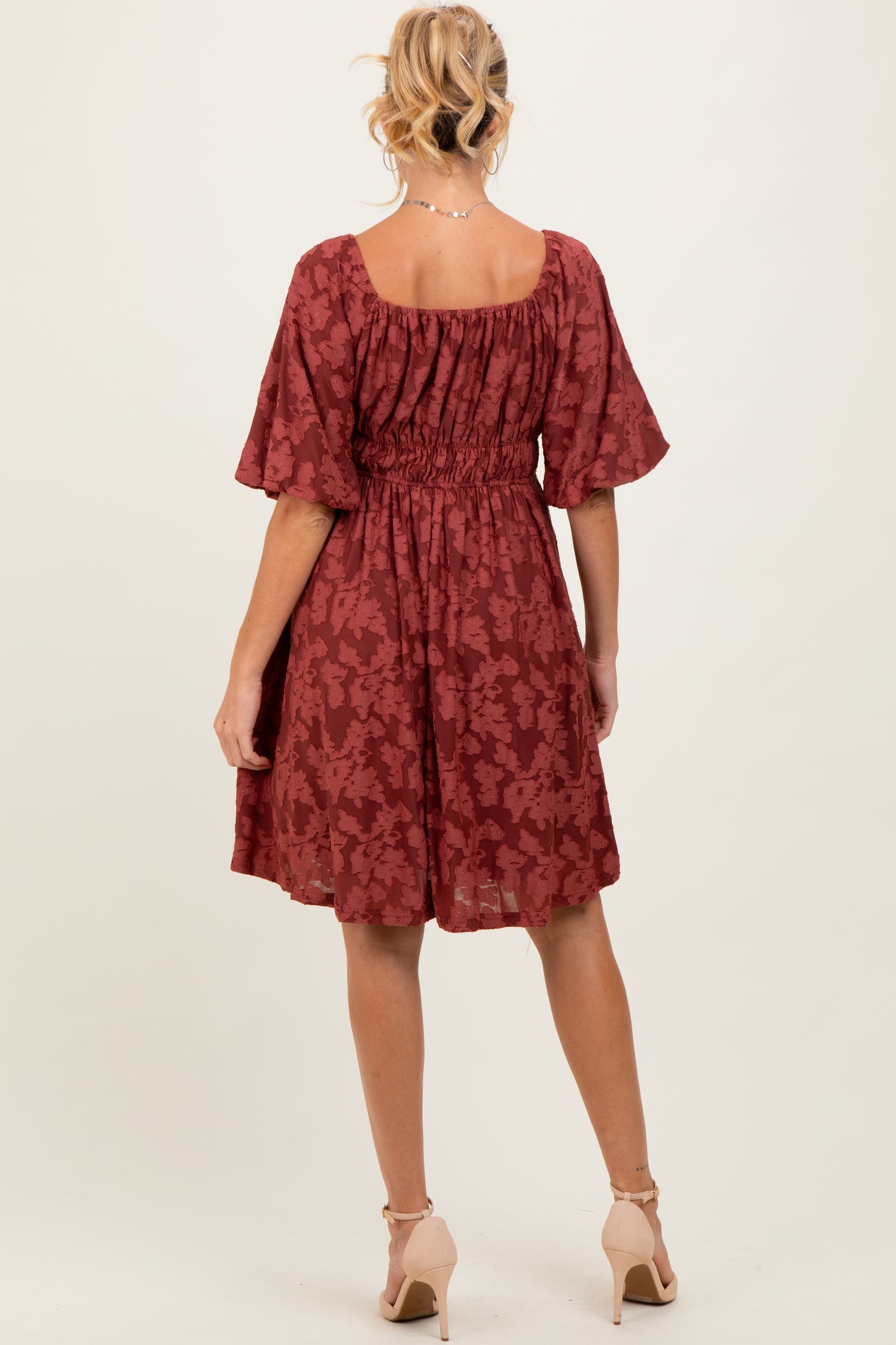 woman wearing a rust floral maternity dress with a smocked waist and short flutter sleeves, showing her baby bump