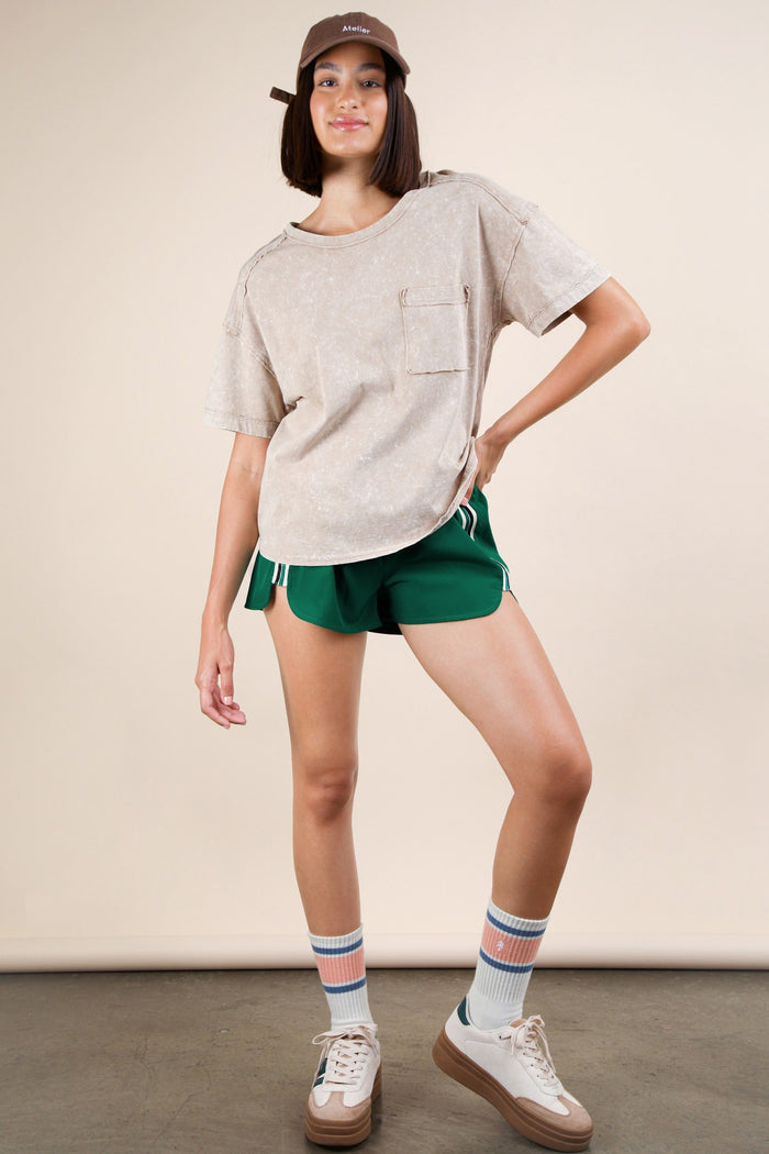 woman wearing a beige oversized t-shirt with a pocket, green athletic shorts, and sneakers with striped socks