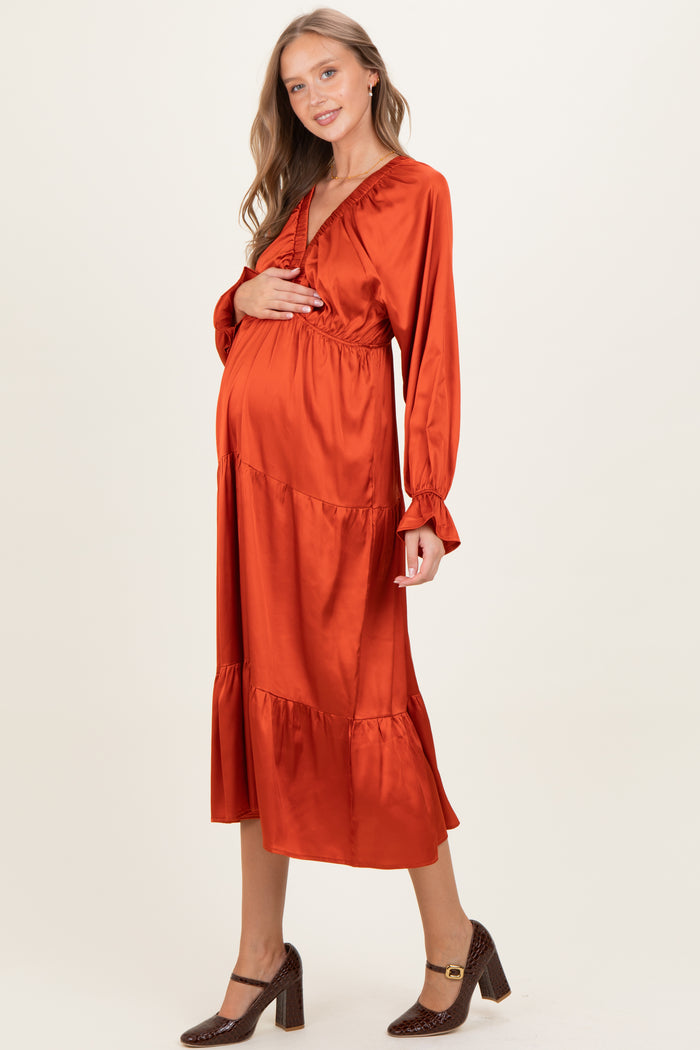 woman wearing an orange maternity maxi dress with long sleeves and a tiered skirt, holding her baby bump