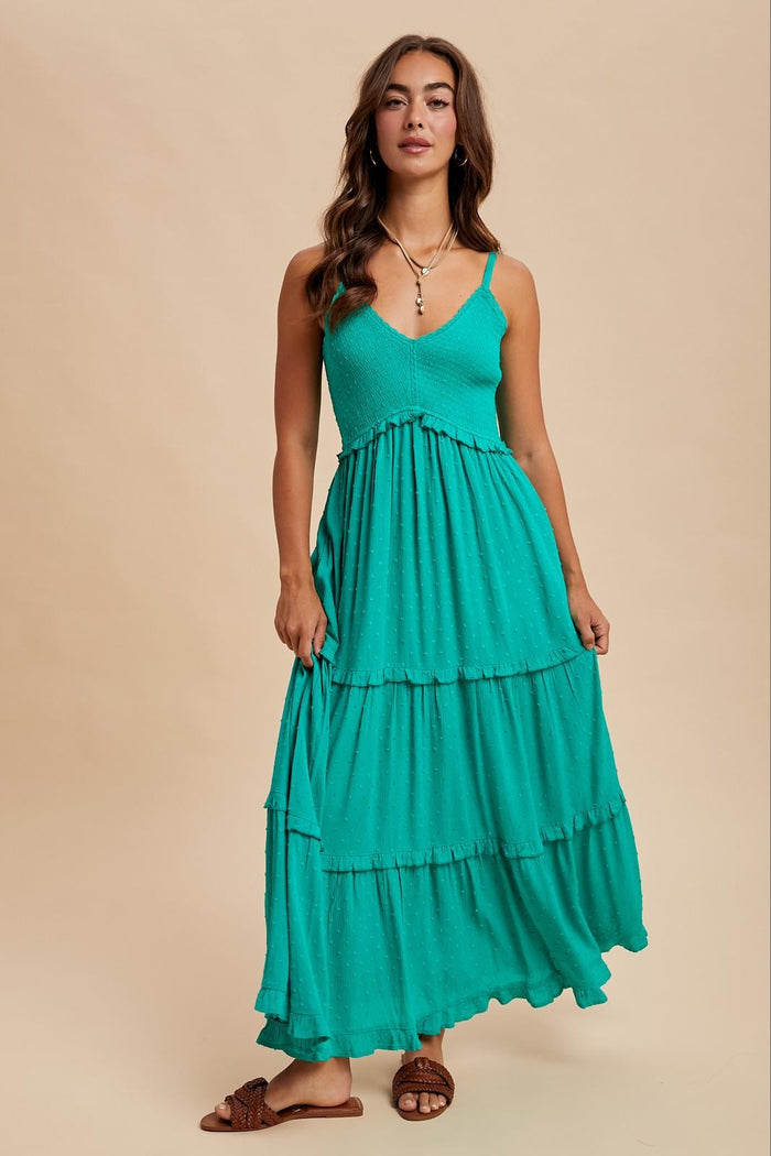 woman wearing a teal tiered maxi dress with thin straps and textured detailing, standing confidently against a neutral background