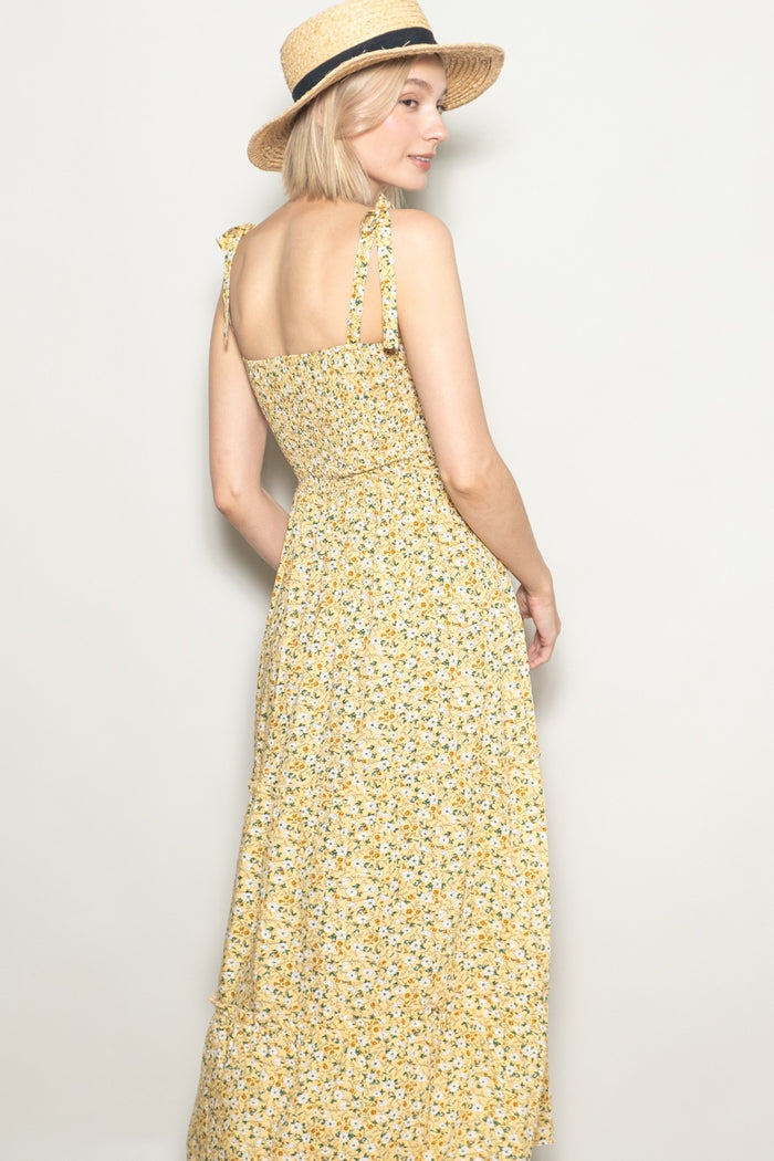 woman wearing a yellow floral maxi dress with shoulder ties and straw hat, turned to show the back view