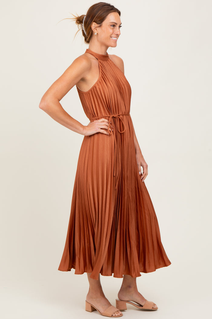 woman wearing an rust-colored pleated maxi dress with a halter neck and tie waist detail