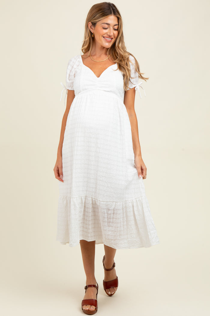 woman wearing a white maternity dress with puff sleeves and a tiered skirt, showing a baby bump
