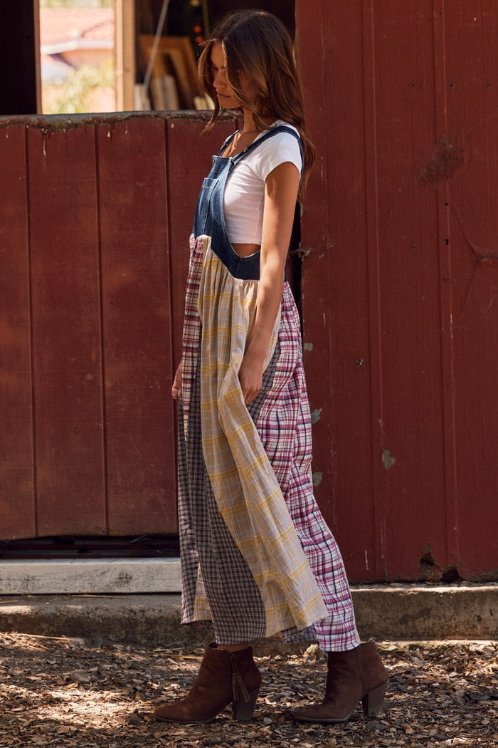 woman wearing a patchwork plaid and denim midi dress with a white t-shirt underneath and brown ankle boots