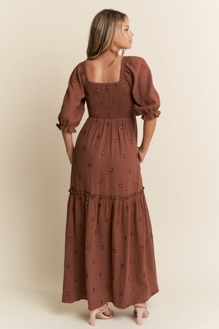 woman wearing a brown floral embroidered maxi dress with a fitted bodice and puff sleeves, showing the back view