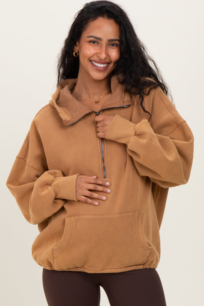 woman wearing a brown maternity pullover hoodie with a half zipper and oversized fit, holding her baby bump