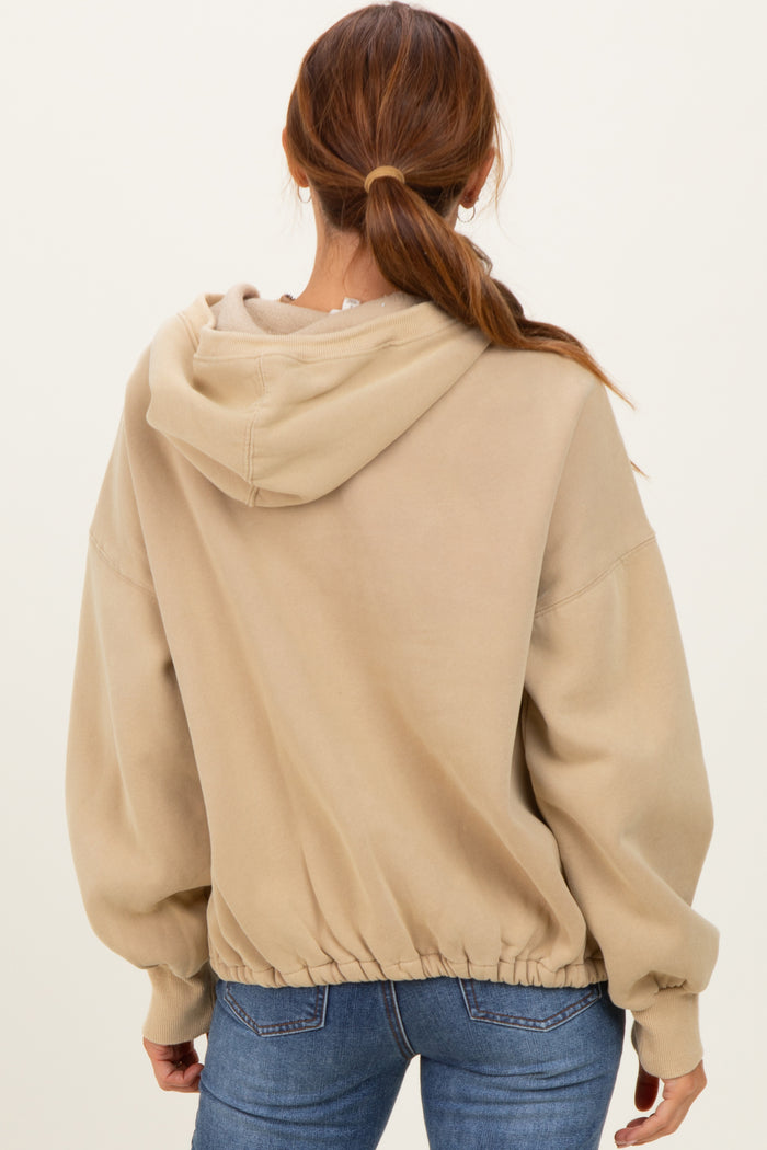 woman wearing a beige oversized hoodie with a cinched hem and a hood, viewed from the back