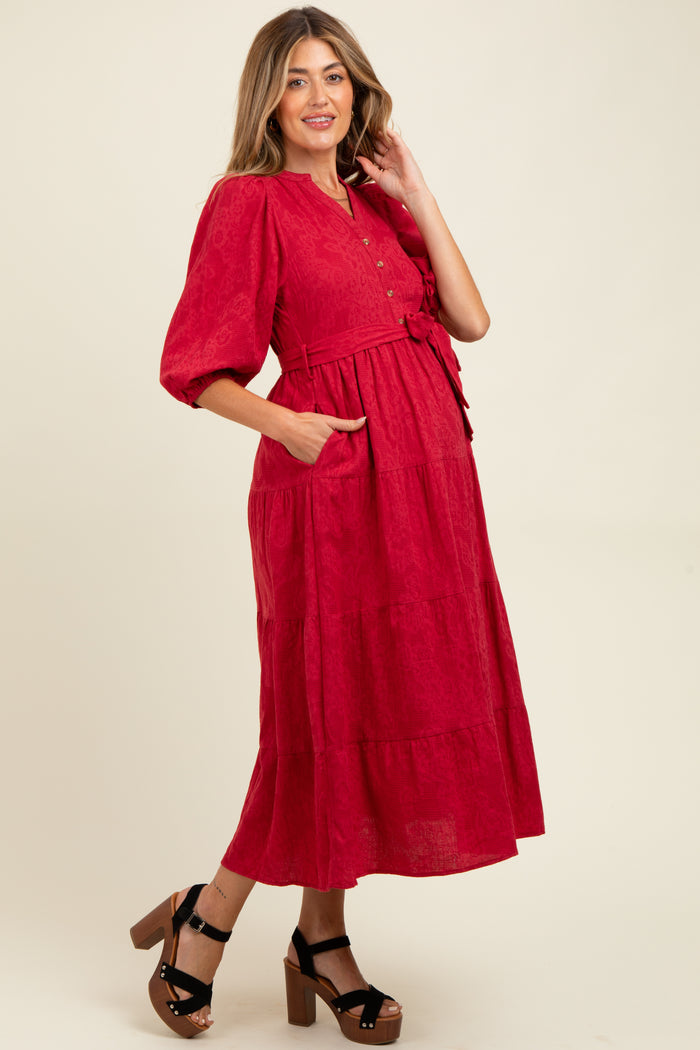 woman wearing a red maternity dress with short puff sleeves, button front, and tie waist, highlighting her baby bump