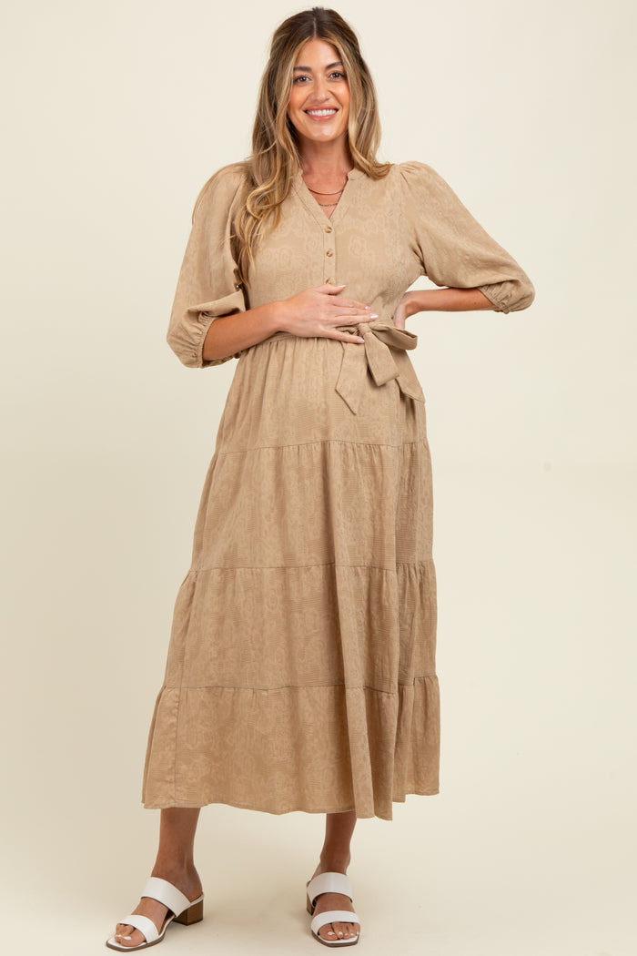 woman wearing a tan maternity midi dress with button details and a tie waist, showcasing her baby bump