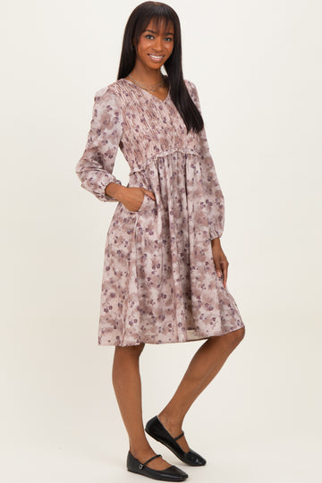 woman wearing a floral smocked midi dress in shades of pink with long sleeves and pockets