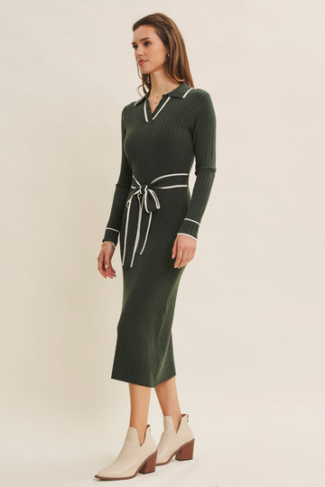 woman wearing a dark green ribbed midi dress with a collar and white trim, cinched at the waist with a belt