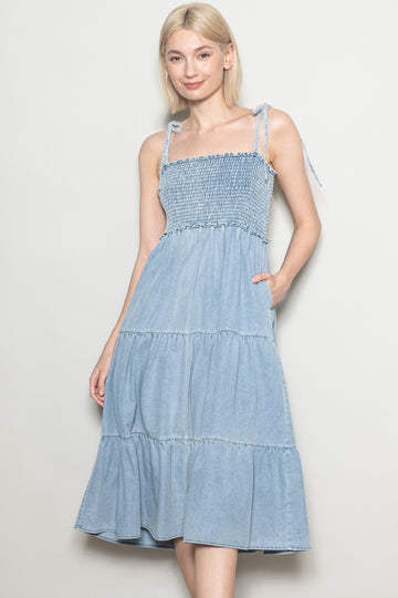 woman wearing a light blue denim sundress with smocked bodice and tiered skirt, featuring adjustable tie straps