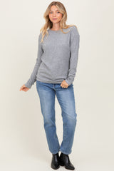 woman wearing a gray long sleeve ribbed top and blue jeans, posed with one hand on her hip