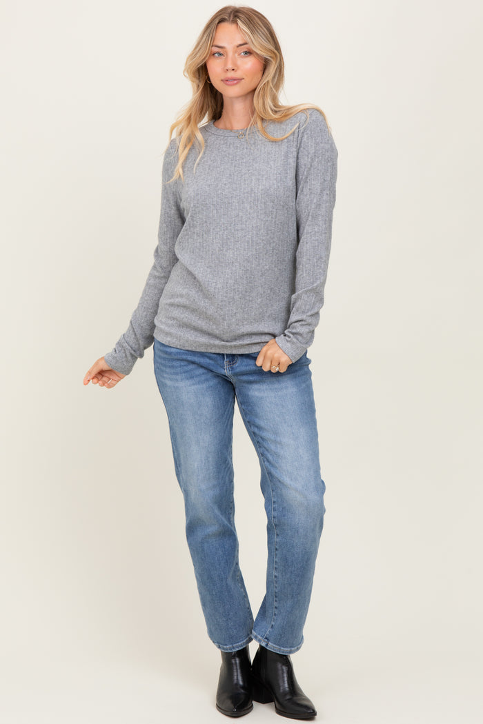 woman wearing a gray long sleeve ribbed top and blue jeans, posed with one hand on her hip