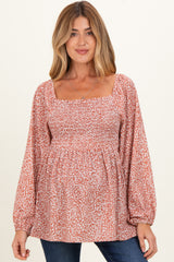 woman wearing a rust floral print maternity top with a square neckline and smocked bodice, showing her baby bump