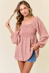 woman wearing a rust-colored smocked top with long puff sleeves and a relaxed fit, paired with denim shorts