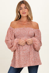 woman wearing a rust off-the-shoulder maternity top with puff sleeves and floral print