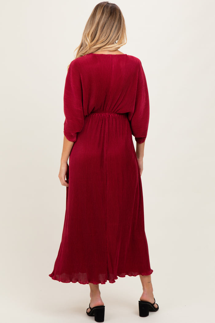 woman wearing a red pleated maternity maxi dress with a cinched waist and three-quarter sleeves, showing her baby bump from behind