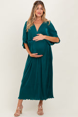woman wearing a teal maternity maxi dress with short sleeves, gently cradling her baby bump