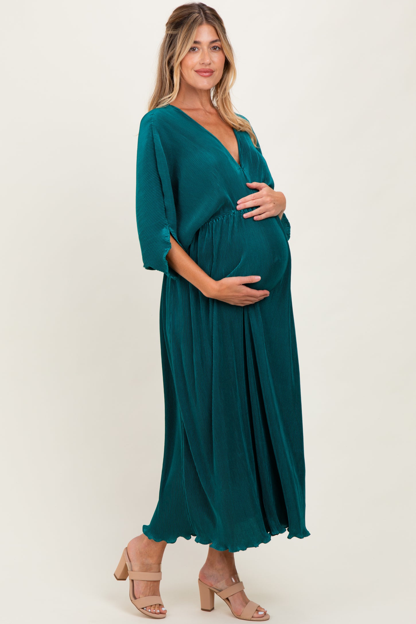 woman wearing a dark teal maternity maxi dress with a v-neckline, gently cradling her baby bump