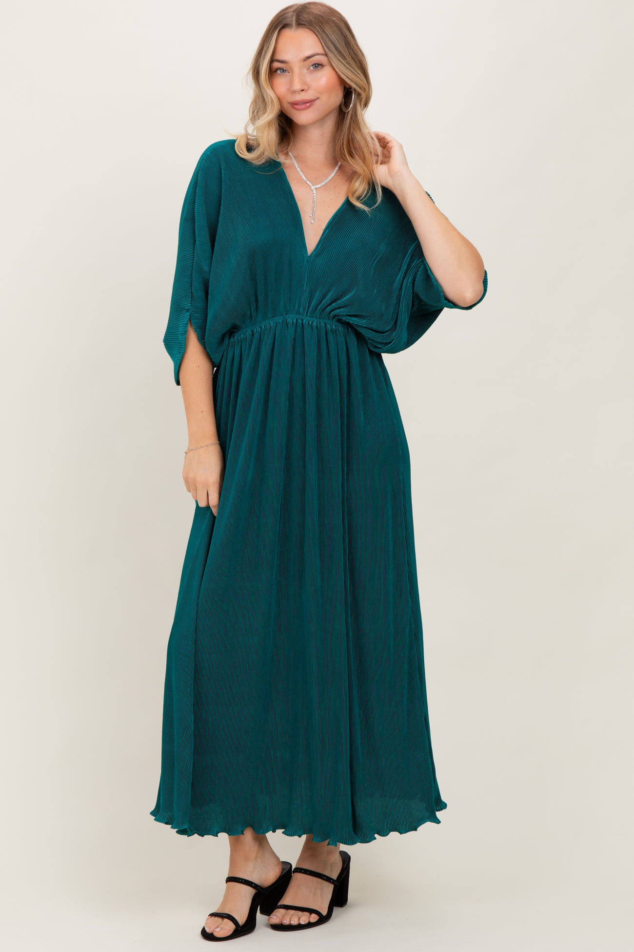 woman wearing a teal maxi dress with a v-neck and short dolman sleeves, standing against a neutral background
