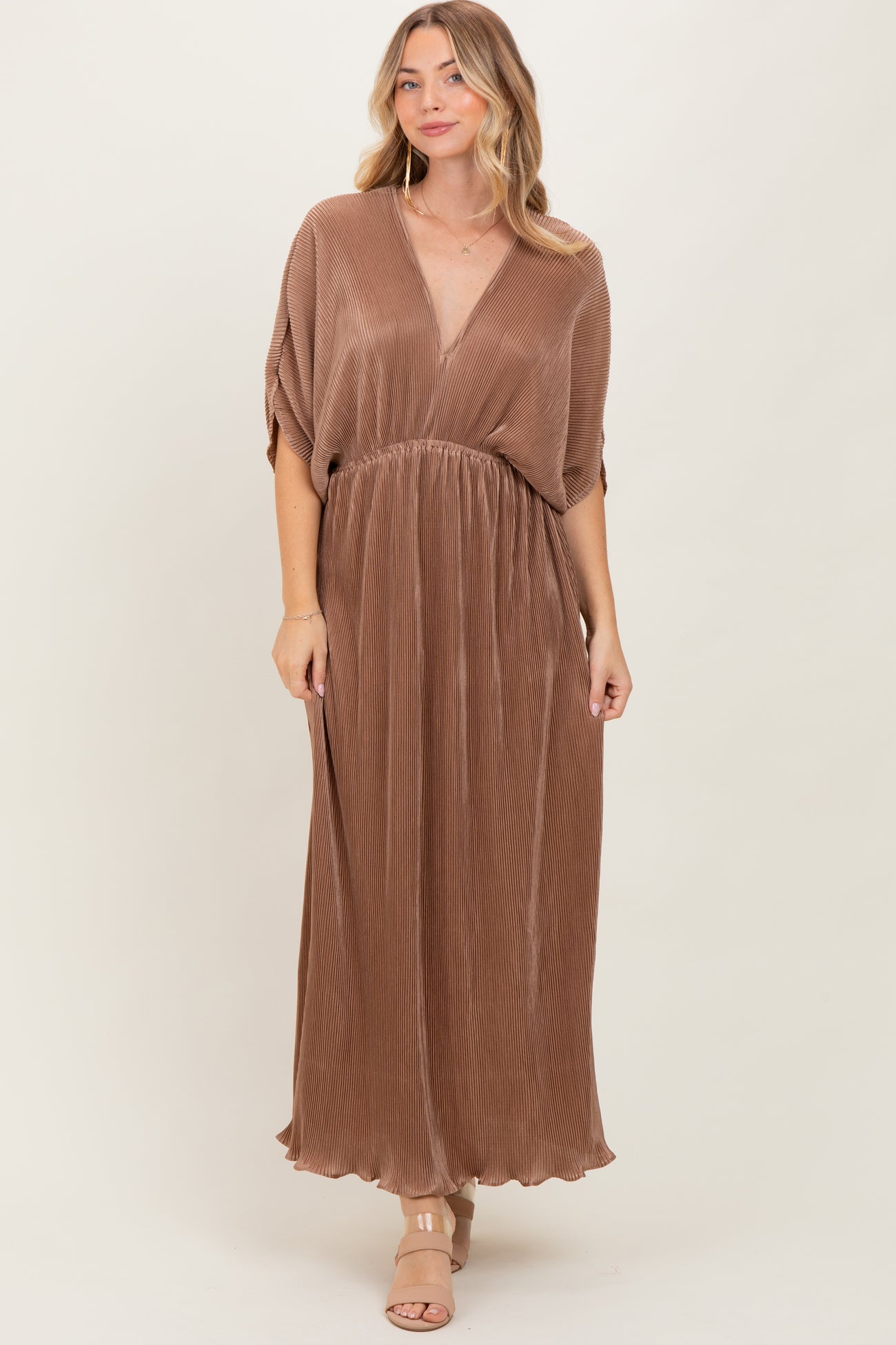 woman wearing a brown pleated maxi dress with a deep v-neck and short sleeves.