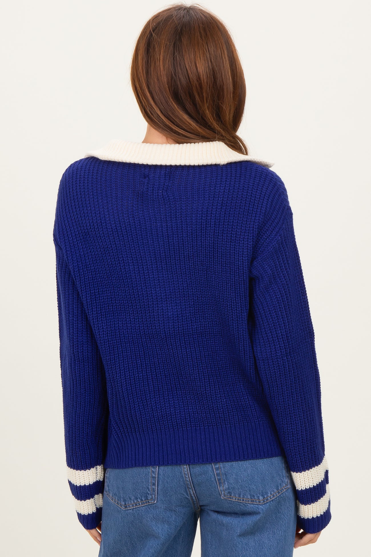 woman wearing a back view of a blue ribbed sweater with a white collar and striped cuffs