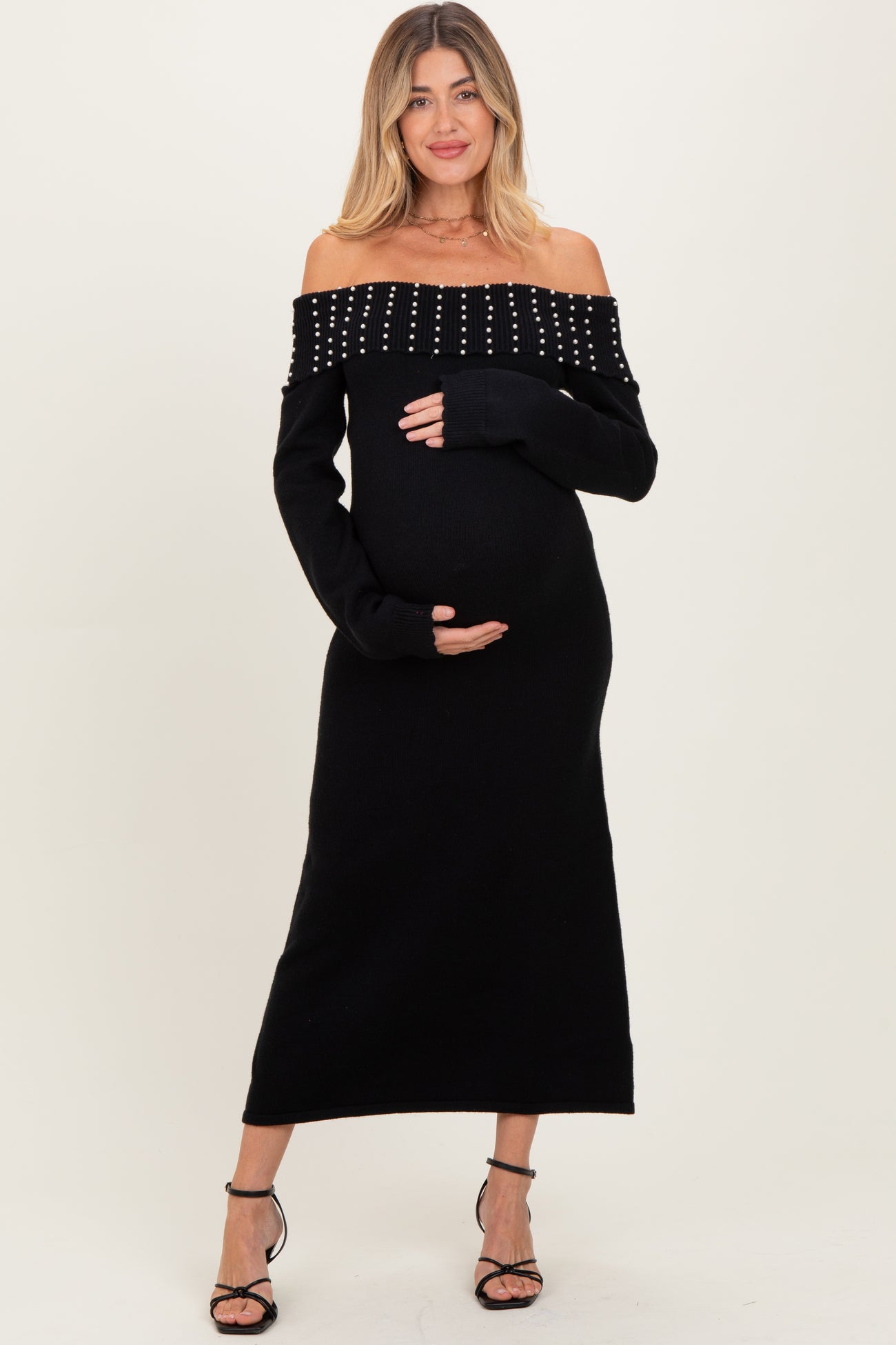 woman wearing a black off-the-shoulder maternity dress with studded details and holding her baby bump