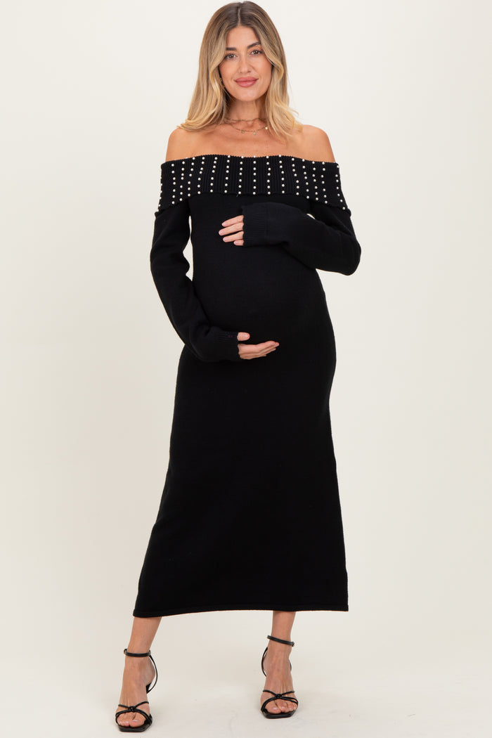 woman wearing a black off-the-shoulder maternity dress with studded details and holding her baby bump