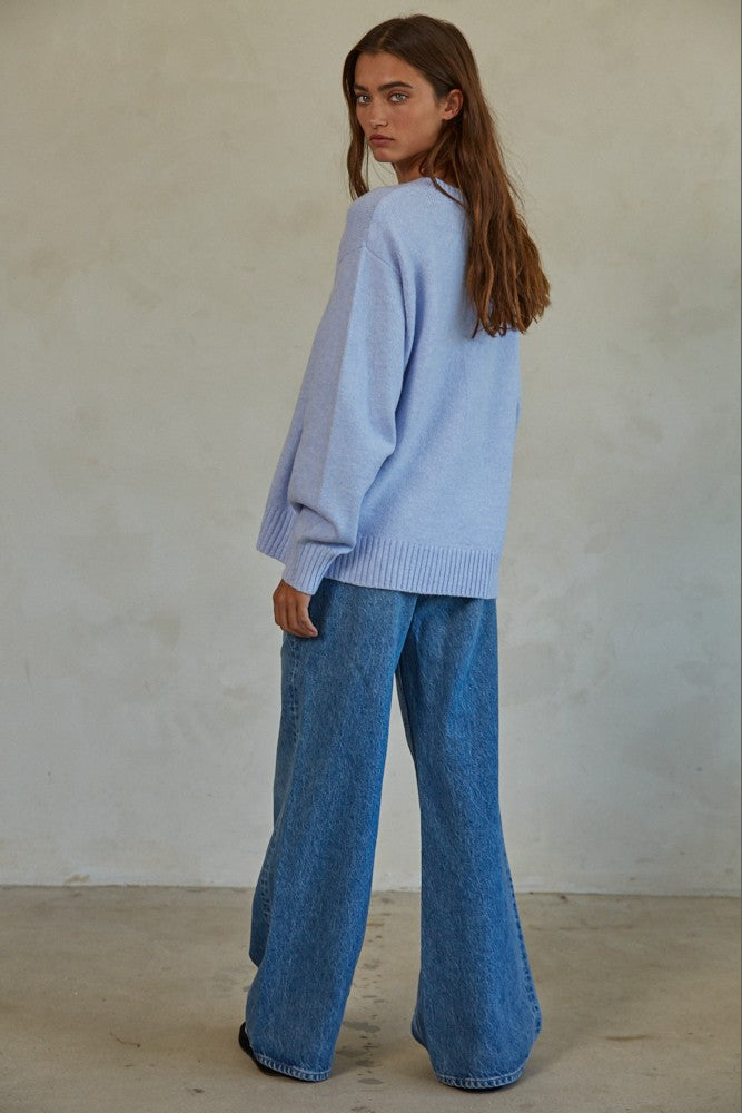 woman wearing a light blue oversized sweater and wide-leg jeans, standing with her back to the camera