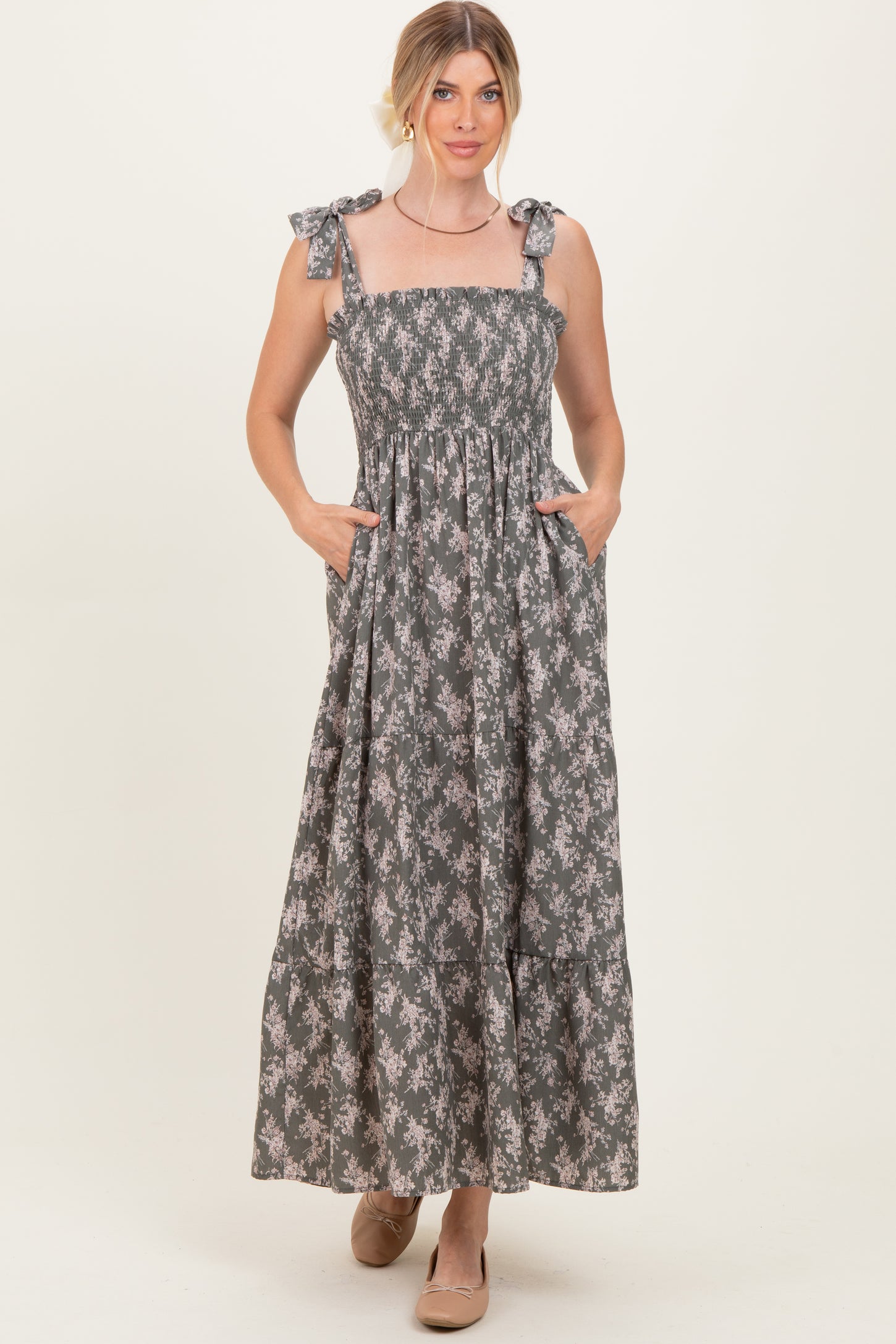 woman wearing a floral print maxi dress with smocked bodice and bow tie straps, featuring pockets
