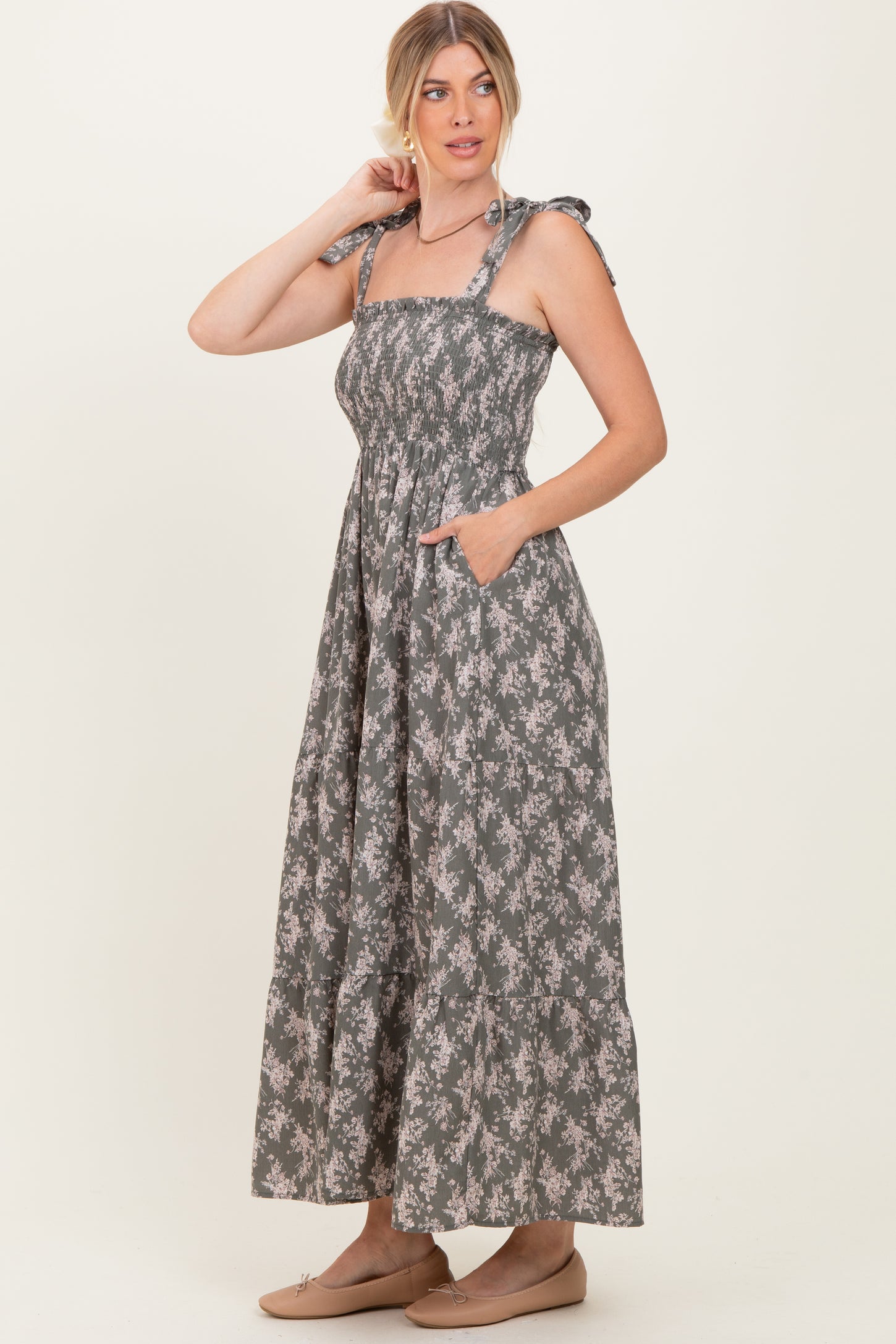 woman wearing a floral print gray maxi dress with smocked bodice and tie straps, featuring pockets