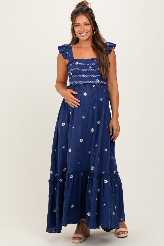 woman wearing a navy blue maternity maxi dress with floral embroidery and ruffled sleeves, showing her baby bump