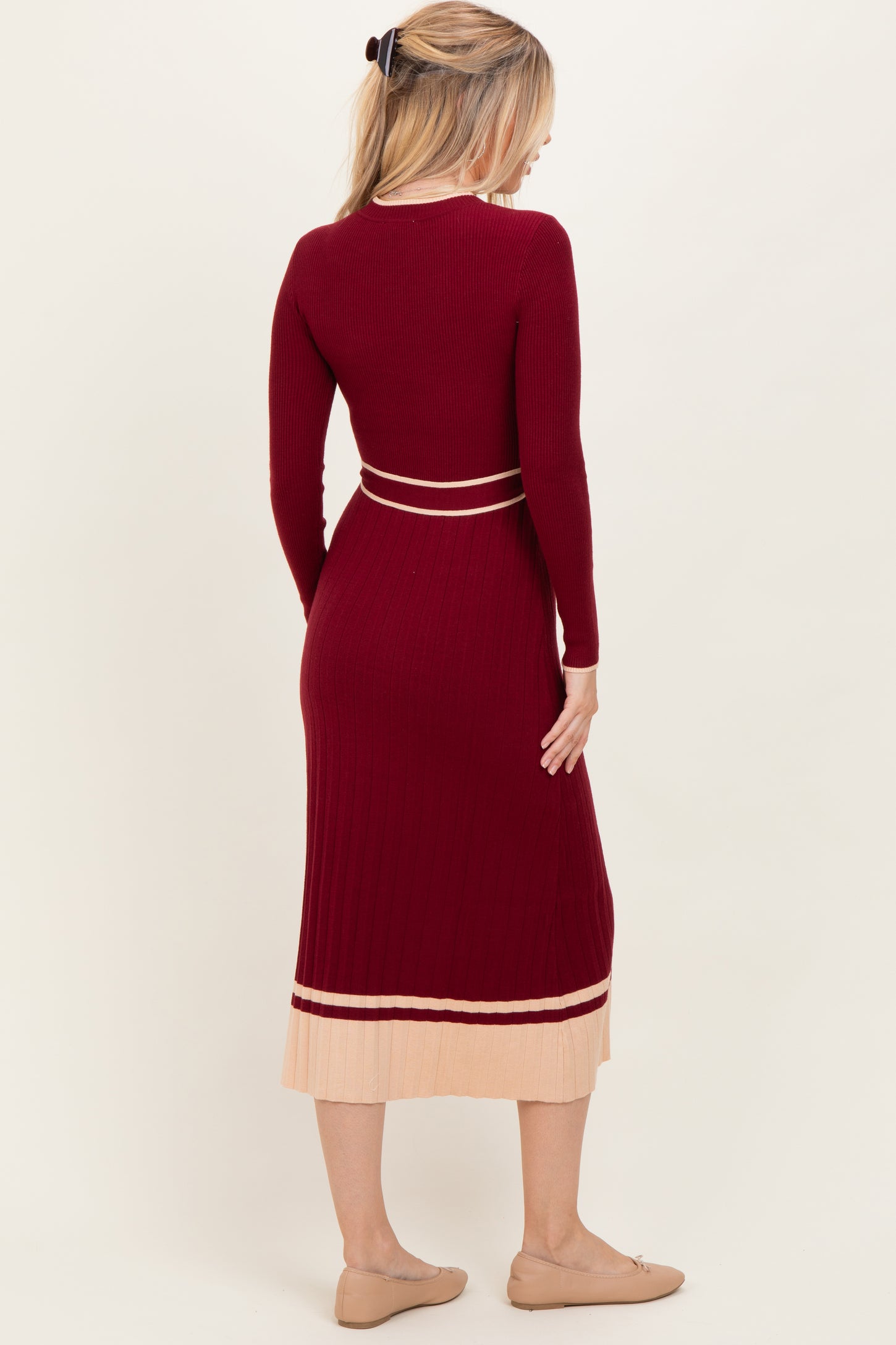 woman wearing a burgundy ribbed long sleeve dress with a beige striped hem and back detail