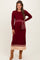 woman wearing a burgundy maternity sweater dress with ribbed texture and a matching tie belt, posing with a smile