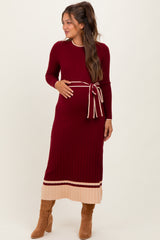 woman wearing a burgundy ribbed maternity dress with a belted waist and contrasting cream-colored stripes, showing her baby bump