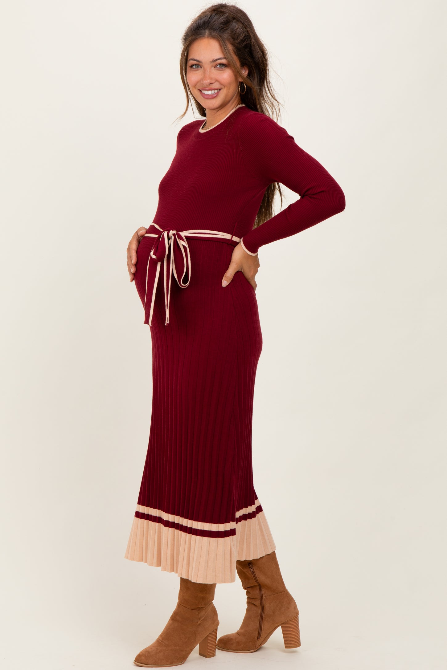 woman wearing a burgundy maternity dress with a tie waist and cream striped hem, showing her baby bump